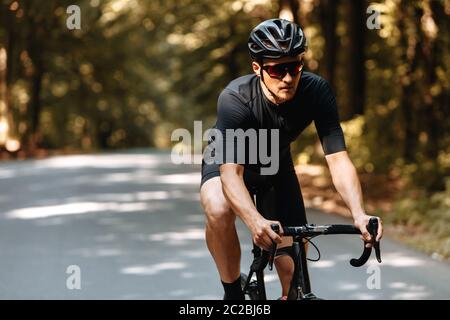 Reifer Mann mit athletischen Körper im Sport-Outfit, Schutzhelm und verspiegelte Glases Reiten Fahrrad im Sommer Wald. Bärtiger Mann, der in Zycl praktiziert Stockfoto