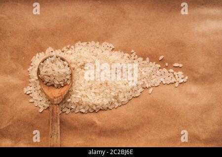 Weißer Reis wird auf einem braunen Hintergrund mit einem Holzlöffel und gegen die andere Kruppe verstreut. cpy Raum Stockfoto
