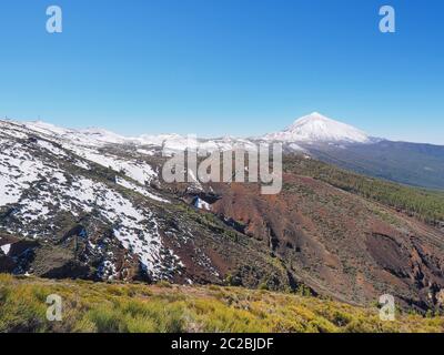 Blick auf eine tolle Vulkanlandschaft, die Montana Roja (rote vulkanische Lavaasche) mit Schnee und frischen Pflanzen im Vordergrund.im Hintergrund kann man Stockfoto