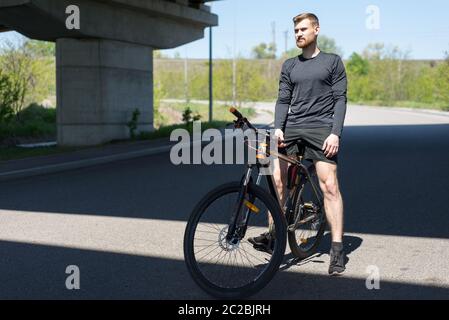 Radfahrer, die auf offener Straße ein Fahrrad fahren, um den Sonnenuntergang-Sportler, bärtigen Radler, Fahrten auf der Autobahn auf einem Sportfahrrad. Unter der Brücke. Im Freien. S Stockfoto