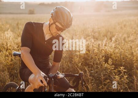 Radprofi in Sportbekleidung, schwarzem Helm und Sportbrille, die Pause vom Radfahren auf der Natur. Müde Mann nach dem Training ausruhen Stockfoto