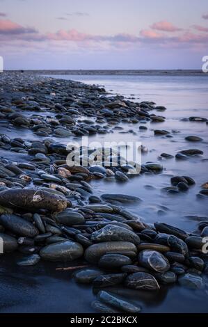 Am frühen Morgen hell über nassen Kieselsteinen in Okarito an der Westküste von Neuseelands Südinsel. Stockfoto