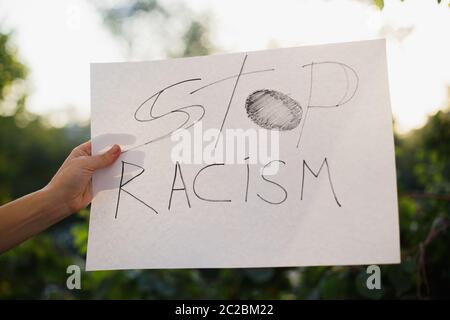 Frau mit weißem Papier mit dem Text "STOP Rassismus". Vor dem Hintergrund von Bäumen und Sonnenlicht Stockfoto