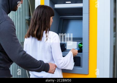 Rückansicht eines Räuber Rucken Karte aus der Frau Hand mit ATM Maschine Stockfoto