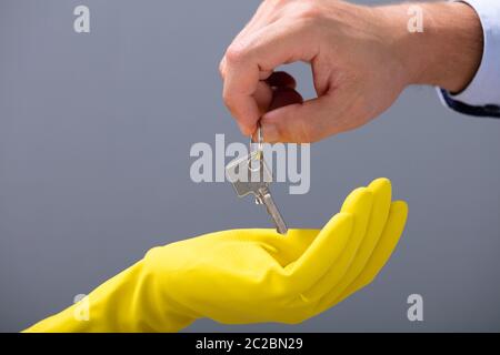 Des Menschen Hand Silber Schlüssel zur Hand Cleaner tragen gelbe Handschuhe gegen grauer Hintergrund Stockfoto