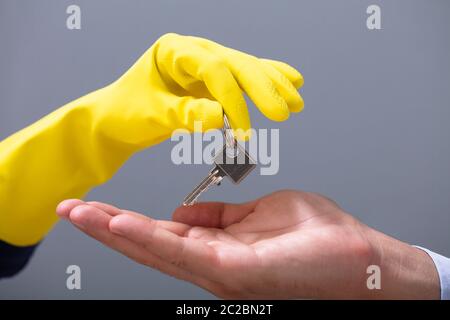 Der Mensch erhält die Schlüssel aus der Hand Cleaner tragen gelbe Handschuhe gegen grauer Hintergrund Stockfoto