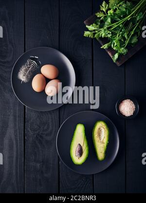 Gekochte Eier, Grün und Avocado mit Himalaya-rosa Salz auf dunklem Holzgrund Stockfoto