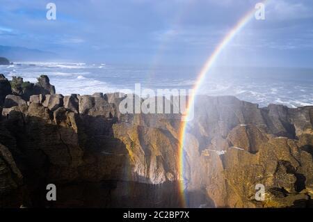 Ein doppelter Regenbogen wird durch Meeresspray in der Luft gebildet, nachdem bei Punakaiki an der Westküste der Südinsel Neuseelands ein großes Blowhole ausbricht. Stockfoto