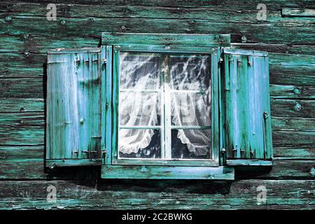 Fenster mit Vorhängen und Fensterläden in einem alten grün-blauen Holzhaus Stockfoto