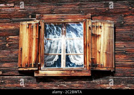 Fenster mit Vorhängen und Fensterläden auf einem alten Holzhaus Stockfoto
