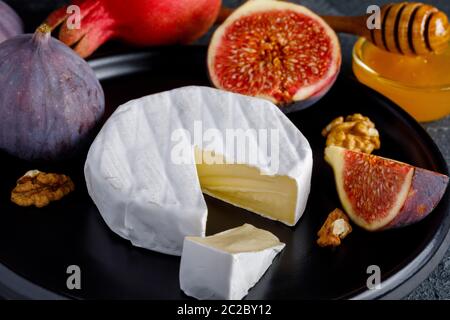 Camembert Käse auf einer Keramikschale mit geschälten Walnüssen und Feigen, Honig und Granatapfel Stockfoto