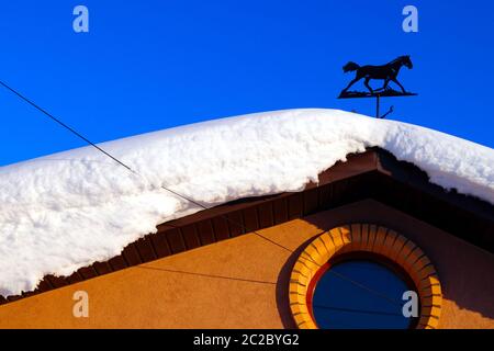 Auf einem Wohnhaus liegt viel Schnee und große Schneeverwehungen. Stockfoto