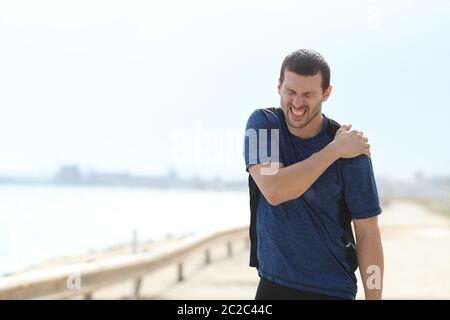 Schmerzhafte Sportler klagen leiden Schulter schmerzen nach dem Sport am Strand Stockfoto