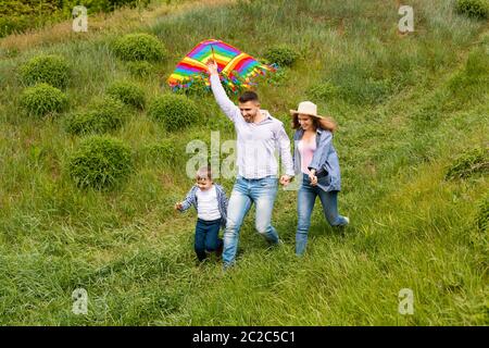 Spaß für die ganze Familie. Junge Eltern mit ihrem Kind fliegen Drachen zusammen auf grüner Wiese Stockfoto