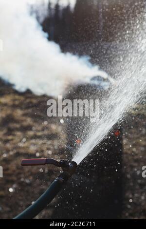 Wasser aus Wasserschlauch in der Nähe Feuer in alten rostigen Fass brennen. Symbol für Brandschutz. Stockfoto