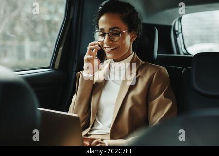 Geschäftsfrau, die mit einem Laptop arbeitet und mit dem Taxi telefoniert. Frau, die auf dem Rücksitz des Autos mit Laptop und Telefon sitzt. Stockfoto