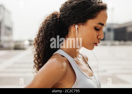 Sportlerin, die im Freien mit Ohrhörern steht. Weibliche Athletin, die nach intensivem Training eine Pause einnahm. Stockfoto