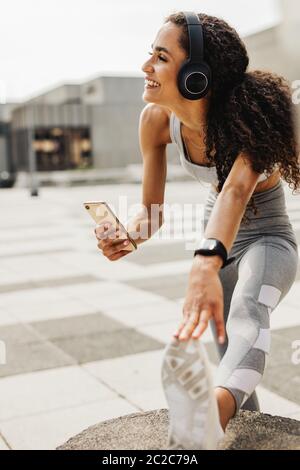 Frau, die in der Stadt trainiert. Frau mit Kopfhörern, die Musik von ihrem Telefon hört. Stockfoto