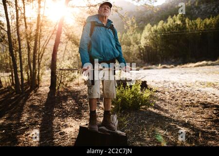 Älterer Mann auf Wandertour steht kein Stein und schaut auf die Bergspitze. Älterer Mann, der eine Pause auf dem Bergweg nimmt, um den schönen Natu zu bewundern Stockfoto