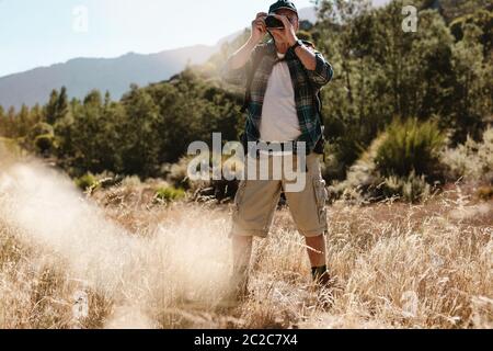 Älterer Mann auf Wandertour, der mit einer Digitalkamera fotografiert. Männlicher Wanderer, der eine Natur fotografiert. Stockfoto