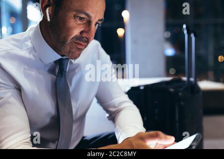 Ein reifer Geschäftsmann in der Flughafenlounge, der das Handy benutzt. Männlicher Geschäftsexperte, der am Flughafenterminal mit seinem Smartphone sitzt und wartet Stockfoto