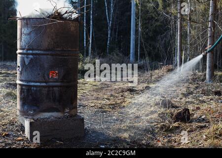 Wasser aus Wasserschlauch in der Nähe Feuer in alten rostigen Fass brennen. Symbol für Brandschutz. Stockfoto