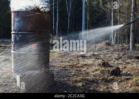 Wasser aus Wasserschlauch in der Nähe Feuer in alten rostigen Fass brennen. Symbol für Brandschutz. Stockfoto