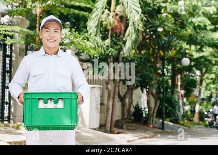 Horizontal Medium Porträt von schönen jungen Lieferung Mann trägt weiße Uniform im Freien stehend hält grüne Kunststoff-Box mit Milchflaschen, Kopie sp Stockfoto