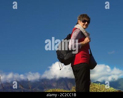 Eine Frau mittleren Alters, sportlich mit einer roten Fleece-Weste und einem schwarzen Rucksack, auf einer Wanderung hoch in den Bergen Teneriffas. Dunkelblauer Himmel und wenig weiß c Stockfoto