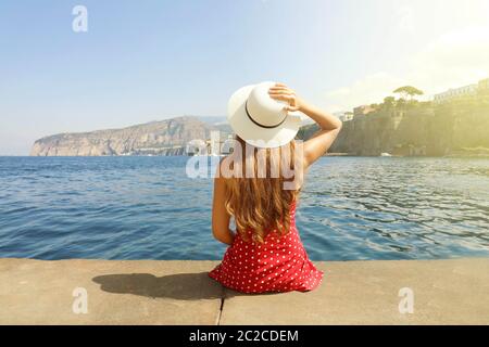 Schöne junge Frau mit Hut sitzt auf der Kante bei herrlichem Panoramablick von Sorrent Dorf auf der Halbinsel von Sorrent, Italien. Stockfoto