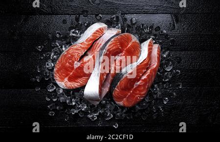 Frischer Lachs Steaks auf schwarzem Holz- Hintergrund. Ansicht von oben Stockfoto