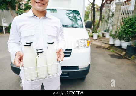 Horizontal mittleren Kopf abgeschnitten Schuss der Lieferung Mann trägt weißes Outfit stehen gegen van ihm hält Milchflaschen, kopieren Raum Stockfoto