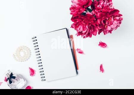 Feminine flache Desktop-Lay mit leerem Notizbuch, Parfüm, Perlenkette und frischen Blumen. Stockfoto