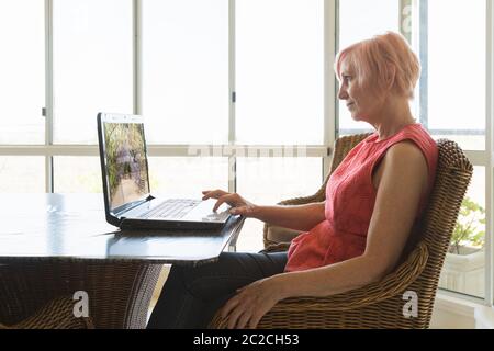 Reife Frau glücklich von zu Hause auf Computer am Küchentisch arbeiten Stockfoto