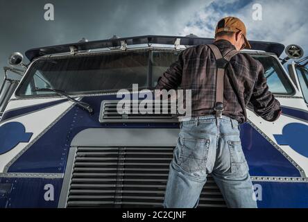 Kaukasischer Commercial Driver in seinen 40er Jahren überprüft LKW Windschutzscheibenwischer in seinem Fahrzeug. Trucker und sein Job. Semi-Wartung. Stockfoto