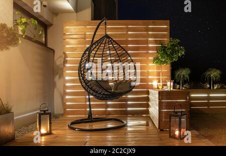 Gartenmöbel Design. Sternennacht im stilvollen Garten mit Holzveranda mit Wand und Blumentöpfe, die von moderner LED-Beleuchtung beleuchtet werden. Stockfoto