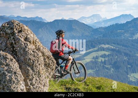 Hübsche Seniorin, die mit ihrem Elektro-Mountainbike bei warmem Sonnenlicht unterwegs ist und den spektakulären Blick über die Allgauer alpen bei Oberstdorf, Ba, genießt Stockfoto