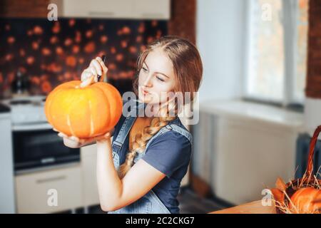 Eine schöne blonde Frau malt Kürbisse für halloween zu Hause in der Küche Stockfoto