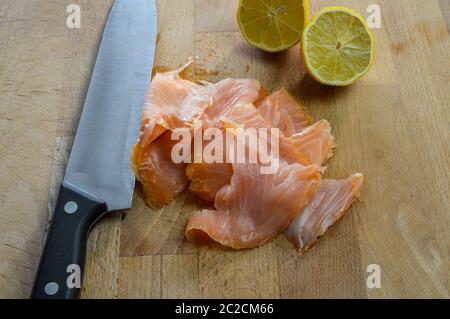 Scheiben von frischem Räucherlachs auf einem Holzbrett mit Küchenmesser und Zitrone aus nächster Nähe. Stockfoto