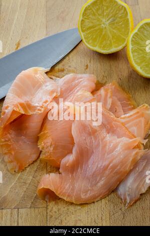 Scheiben von frischem Räucherlachs auf einem Holzbrett mit Küchenmesser und Zitrone aus nächster Nähe. Stockfoto