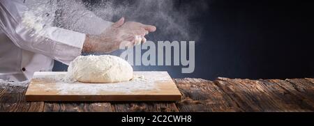 Koch oder Bäcker abstauben ein Haufen ungekochten Teig mit Mehl in der Luft durch Händeklatschen in einem rustikalen Panorama Banner mit Kopie Raum ausgesetzt Stockfoto