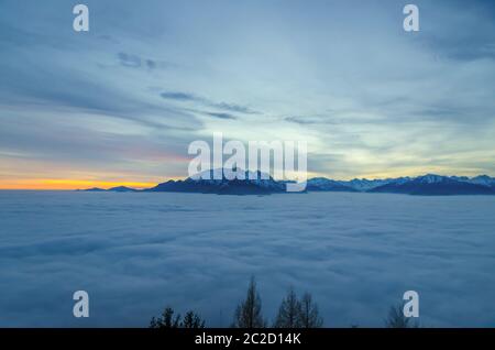 Luftaufnahme über Wolkenlandschaft und schneebedeckten Berggipfel bei Sonnenuntergang mit buntem Himmel in der Schweiz. Stockfoto