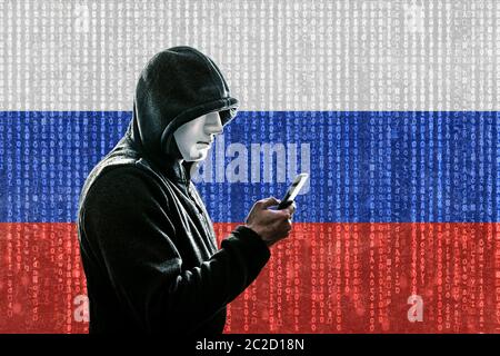 Russische Hacker mit Maske mit Kapuze holding Smartphone Stockfoto