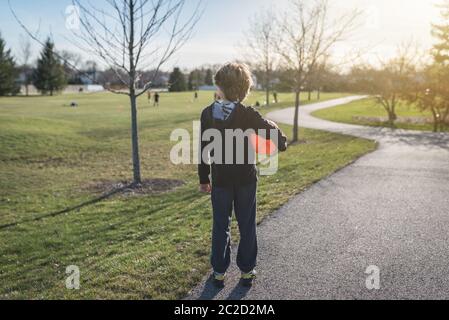 Rückansicht eines Kindes, das einen leuchtend orangefarbenen Fußball in einem Park hält Stockfoto