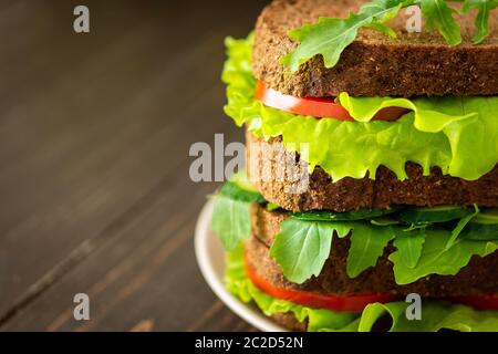 Sandwiches mit Salat und Rucola, Tomaten und Gurken, vegane Sandwiches aus grobem dunklem Brot mit frischem Gemüse Stockfoto