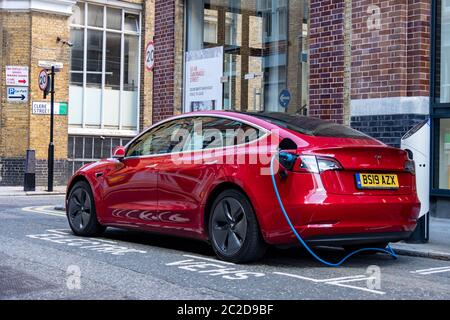 LONDON, JUNI 2020: Ein roter Tesla Model 3 parkte und lad auf der City Street Stockfoto