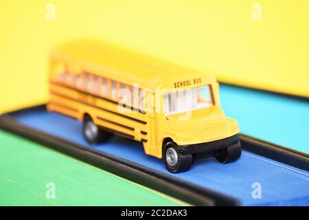 Nahaufnahme von einem Spielzeug School Bus auf einem Buch mit Blau gesprüht Kanten auf gelben Hintergrund. Stockfoto