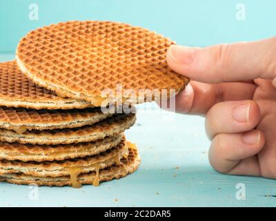 Hand hält Stroopwafels. Hand mit Karamell Dutch Waffel Nahaufnahme auf türkisfarbenem Holzhintergrund Stockfoto