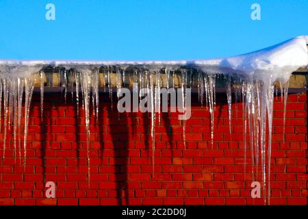 Viele große und scharfe Eiszapfen hängen auf dem Dach des Hauses. Stockfoto