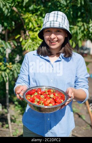 Frau hält eine Schüssel frisch gepflückter Erdbeeren in den Händen und lächelt Stockfoto